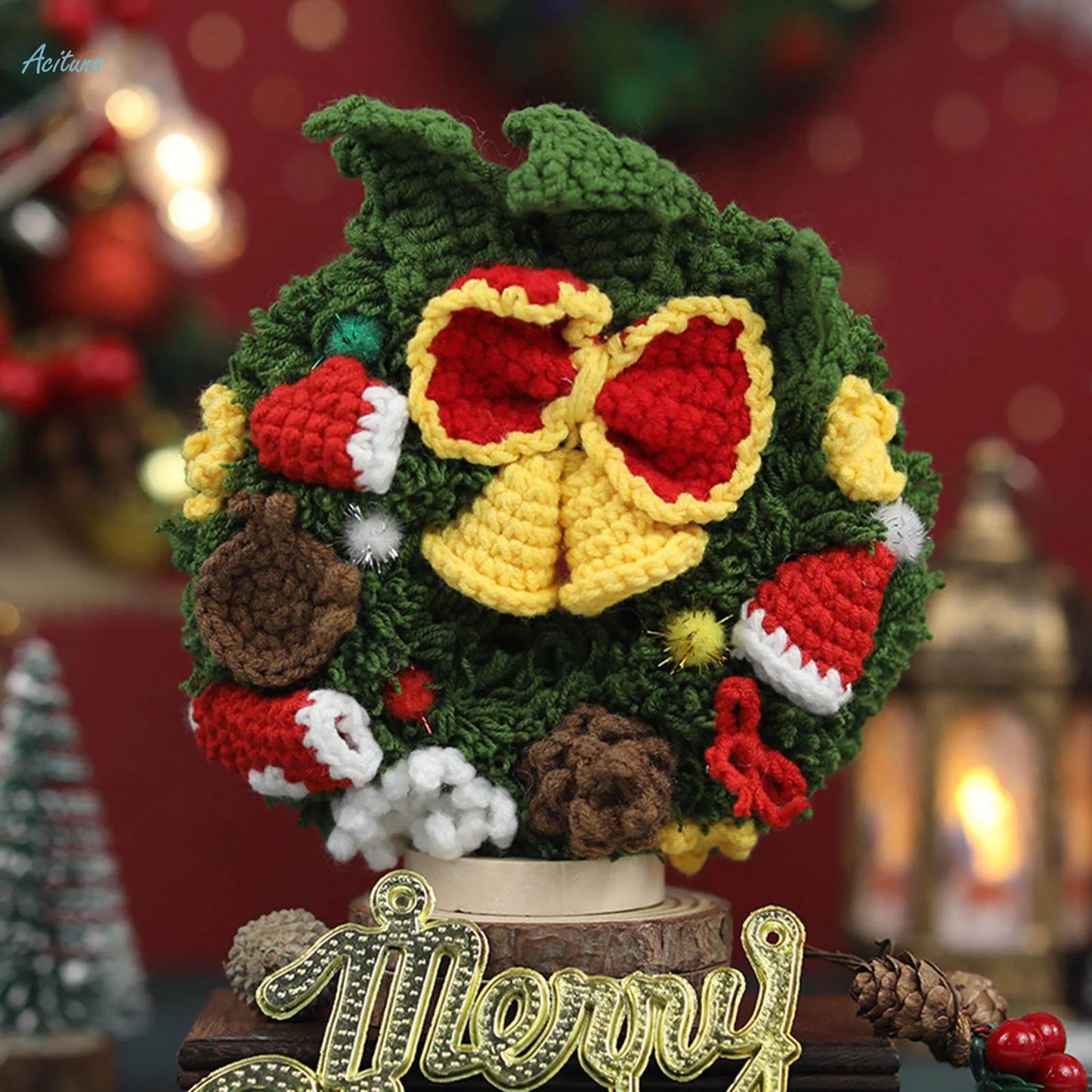 Crocheted Christmas wreath with a red and yellow bow on a wooden stand with 'Merry' sign, blurred festive background.